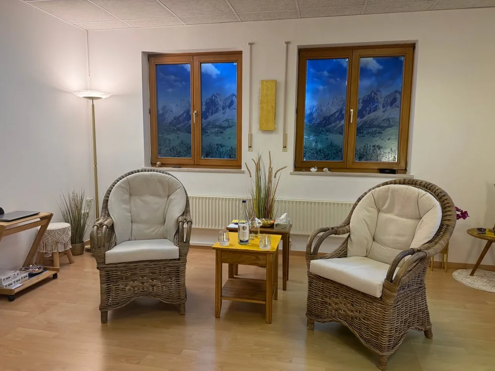 Zwei geflochtene Sessel mit Kissen vor Fenstern mit Bergpanorama